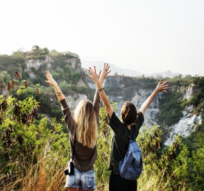 two women standing on a cliff raising their arms